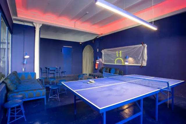 A blue room with a ping pong table, a low sofa and a long neon tube