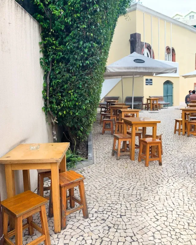 A stone-paved yard with wooden tables and stools, an ivy-covered wall and a white parasol
