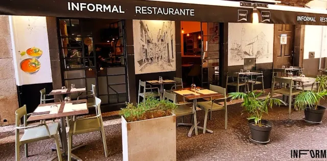 Outdoor tables with metal chairs in front of a dark facade with sketch drawings
