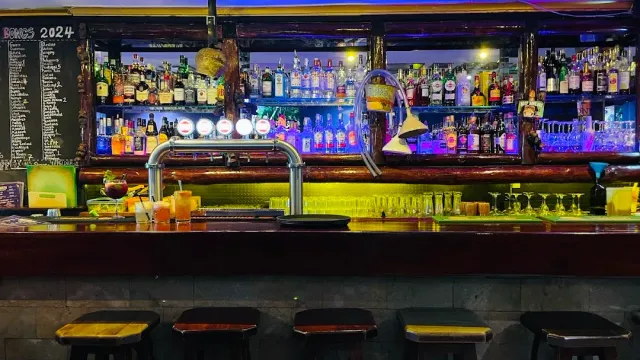 A long bar counter with taps, bottle shelves and colorful lighting