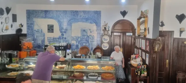 A display counter with pastries, a wall of painted blue tiles and people behind the counter
