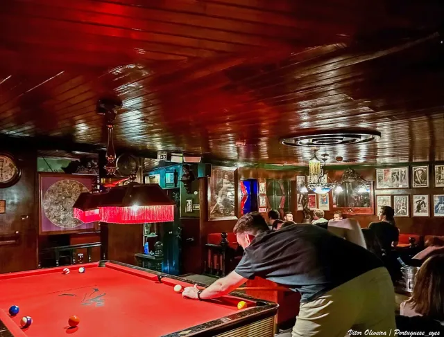 A dim wood panelled bar with a pool table under red light
