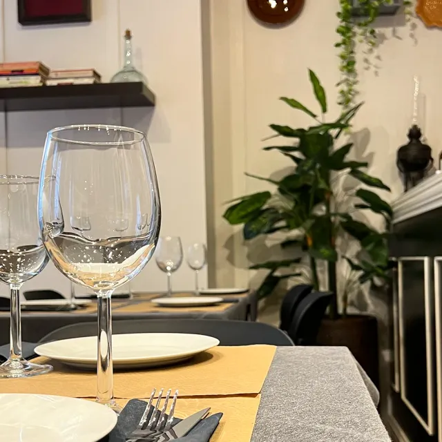 Empty wine glasses on a set table, a green plant and a bookshelf in the background