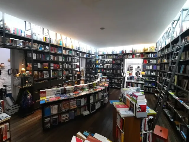 A bookshop with tall loaded shelves, a metal ladder, a wooden floor and stacks of books