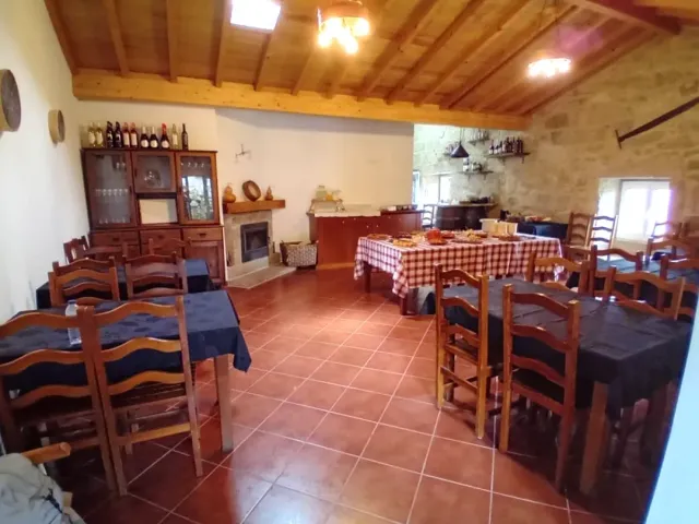 A rustic hall with a terracotta floor, a stone wall, a fireplace and tables in chequered cloths