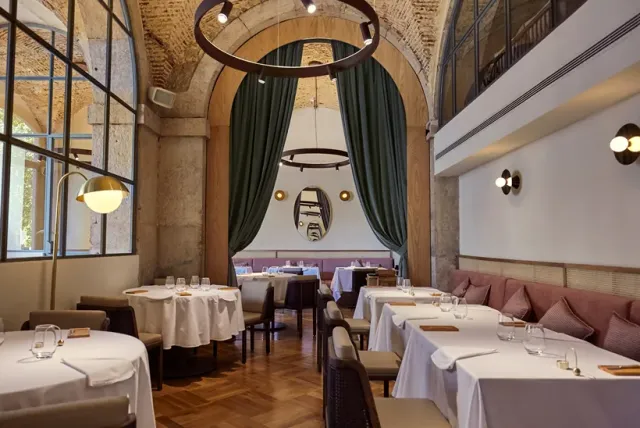 A tall dining room with stone arches, a green curtain and tables in white cloths