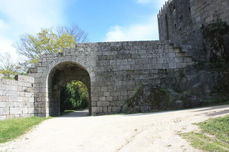 A stone arched gate in a granite wall with a crenellated tower behind