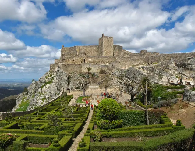 A stone fortress on a rocky hilltop above clipped box gardens