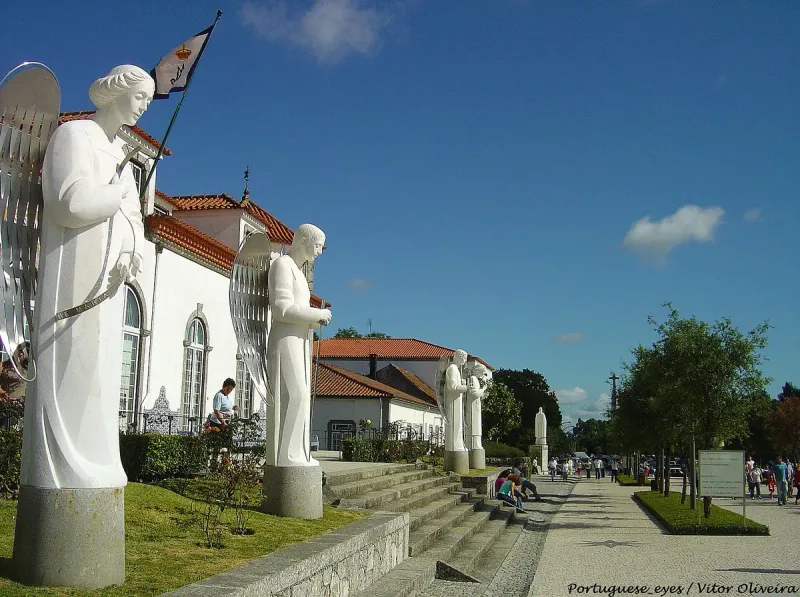 White angel statues along a stone esplanade facing a white building with a tiled roof