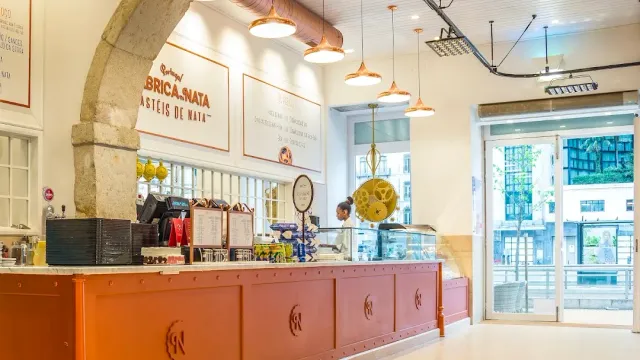 A bakery space with a long orange counter, hanging copper lamps and a stone arch