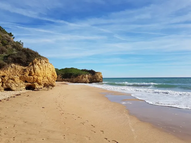 A golden sand beach framed by yellow cliffs, with gentle waves and blue skies