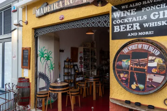 A yellow front with an open door, barrel tables and a black drinks sign