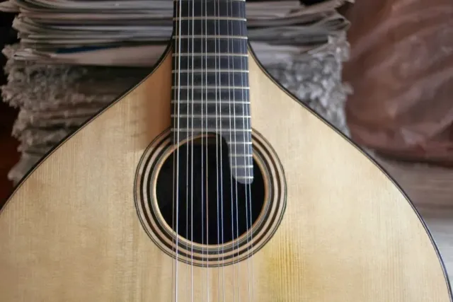 A close up of a pale Portuguese guitar body with strings and a decorated sound hole