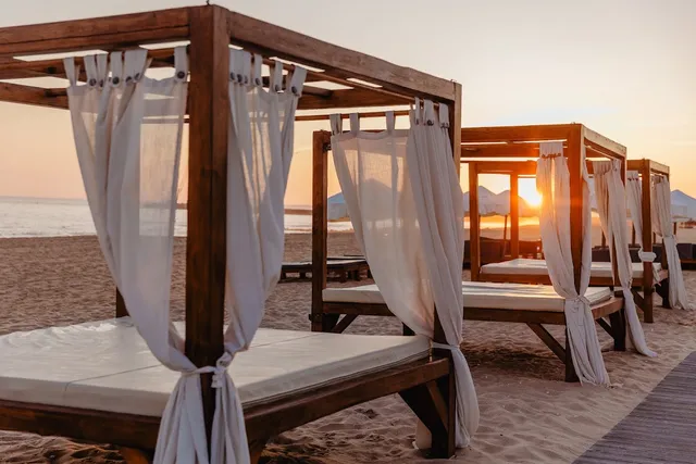 Wooden beach beds with white curtains on the sand at sunrise or sunset