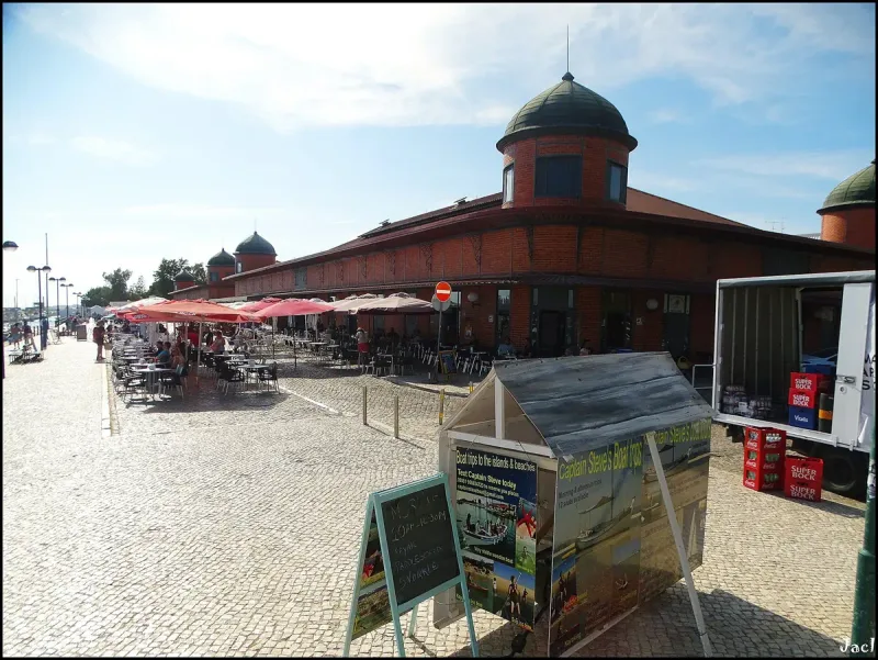 A red brick market hall with a green turret and red parasols alongside