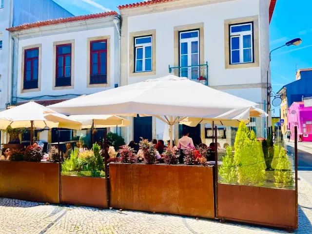 A street terrace with large white parasols, planters and white houses behind