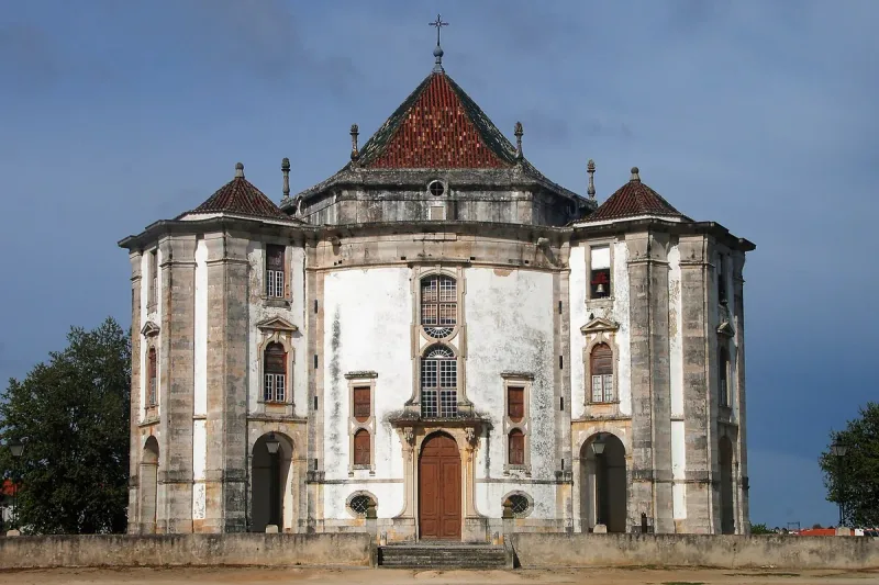 A whitewashed octagonal church with red tile roofs and corner turrets, against dark skies
