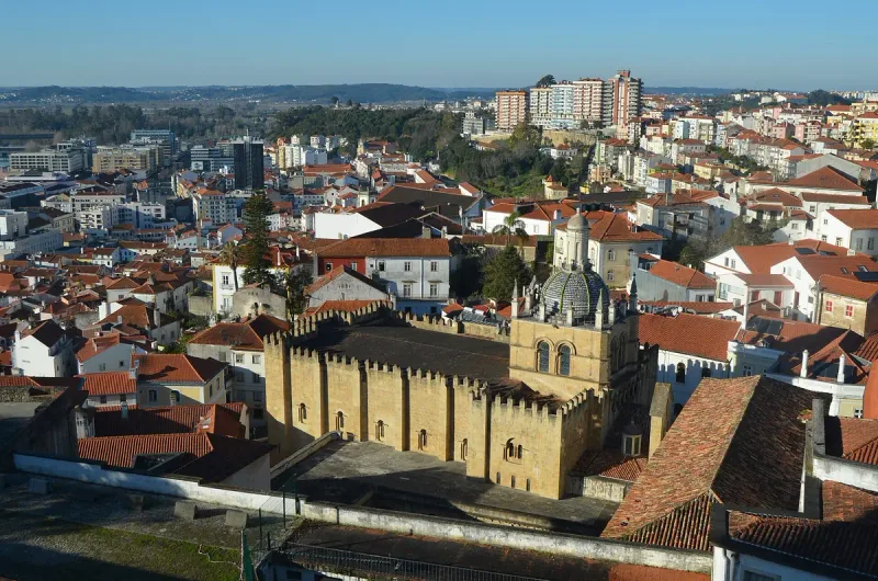 Fortress like stone building with a crenellated wall amid a hillside city of tiled roofs