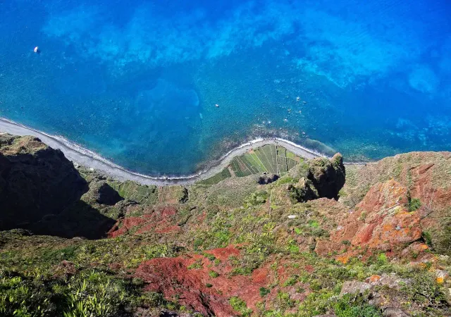 A sheer view down to green terraces and a shoreline above deep blue water