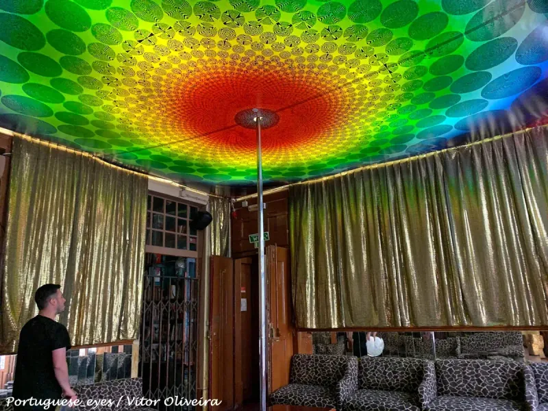 A bar room with a circular rainbow patterned ceiling, gold curtains and leopard print sofas