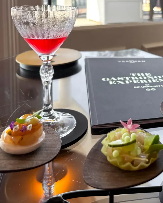 Two flower garnished tasting plates beside a red cocktail and a bound menu