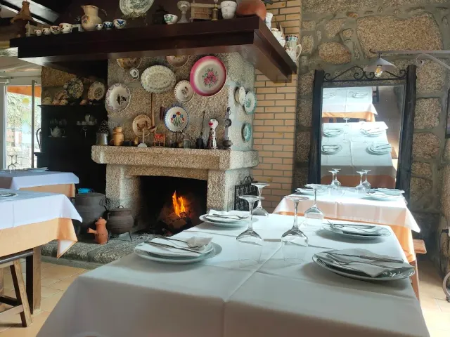 A large stone fireplace with a burning fire and decorative plates, facing white clothed tables