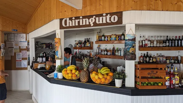 A white bar counter with baskets of tropical fruit and bottle shelves under a wooden ceiling