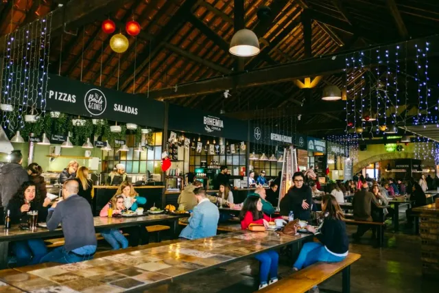 A stall hall with long wooden tables, food signs and strings of lights from the ceiling