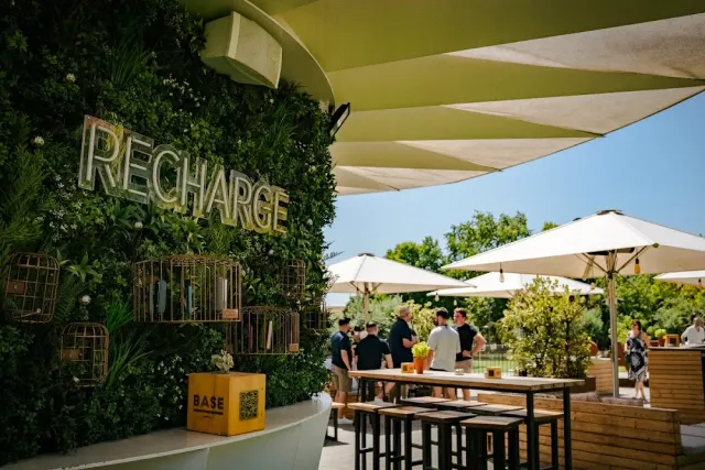 A plant wall with an illuminated sign, shade sails and high tables in a garden