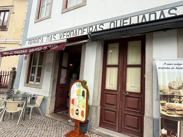 A shopfront with a long awning, brown wooden doors, an ice cream sign and chairs outside
