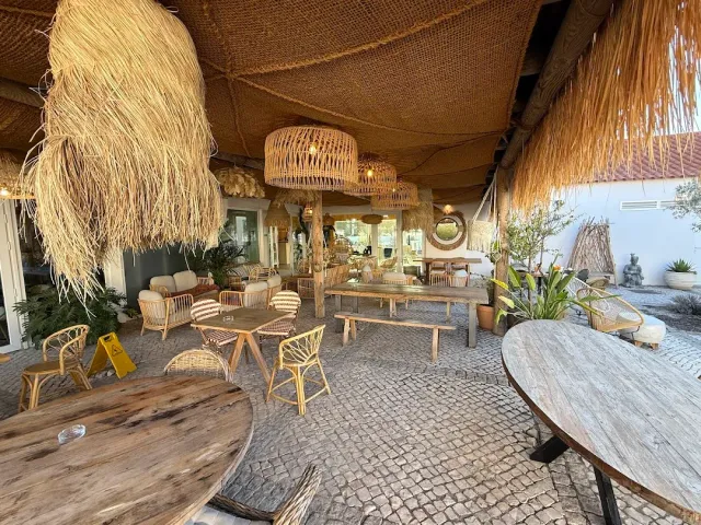 A thatch-covered terrace with straw lamps, rattan furniture and wooden tables on stone