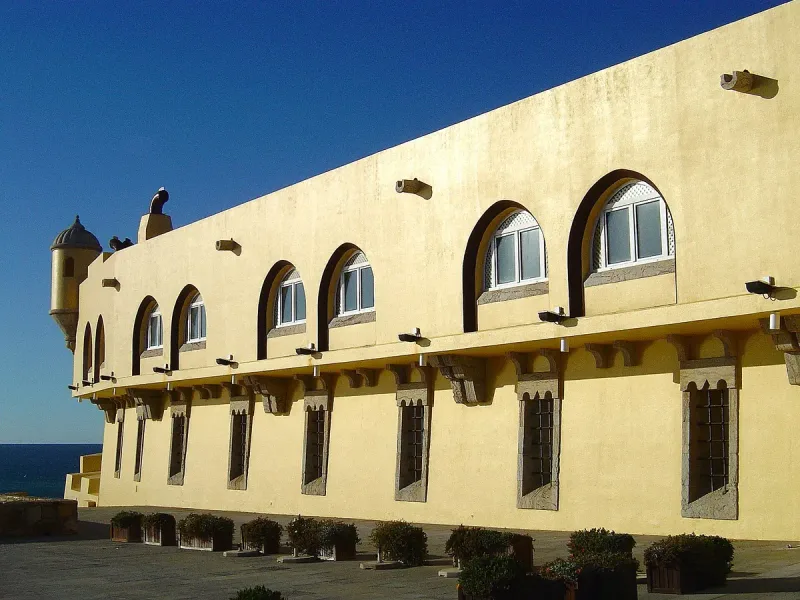 Sand coloured fortress walls with arched windows and a watchtower facing the sea