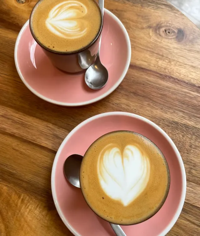 Two cups of coffee with hearts drawn in the foam, on pink saucers and a wooden table