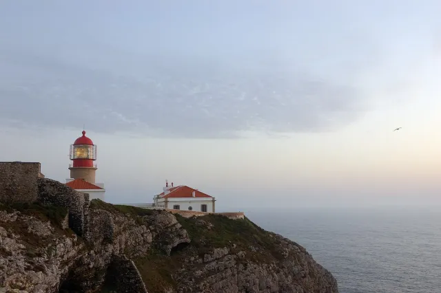 A red lighthouse on a high clifftop above the ocean