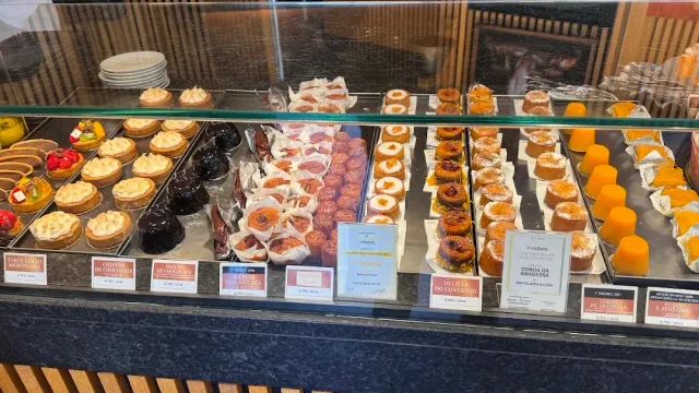 A glass display case with rows of cakes, tarts and orange sweets and price labels