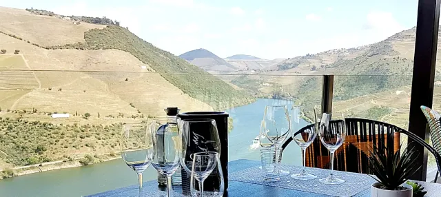 Wine glasses and a bottle on a terrace table, facing a river between arid hills