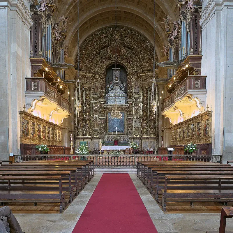 A church interior with a gilded, carved altar, wooden pews and a red carpet down the centre aisle