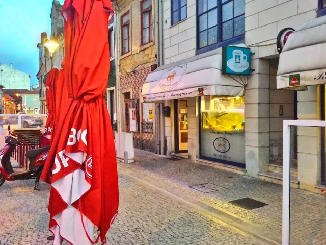 A paved street at dusk with a closed red parasol and a lit restaurant front