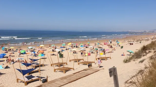 A wide sandy beach with umbrellas, sun loungers and a wooden path to the waves