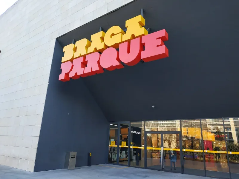 Dark shopping centre facade with a large three dimensional sign in yellow and pink above glass doors