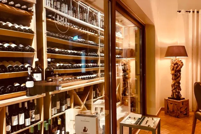 Wooden shelves loaded with wine bottles beside a lamp with a dark shade
