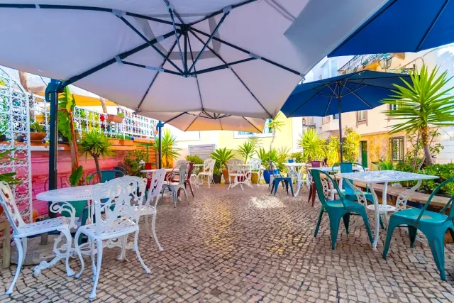 A stone paved courtyard with white and blue parasols, white iron chairs and potted plants