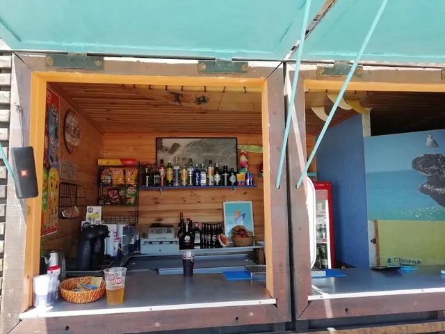 An open wooden kiosk with a bottle shelf and a glass of beer on the counter