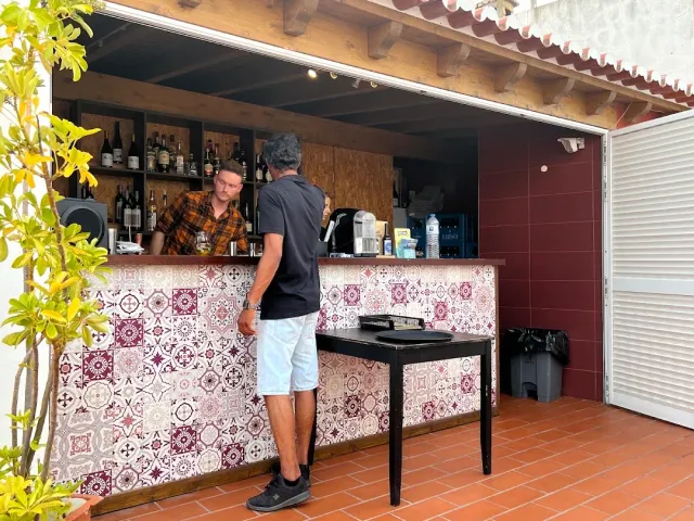 An outdoor counter clad in patterned tiles with bottle shelves and two people beside it