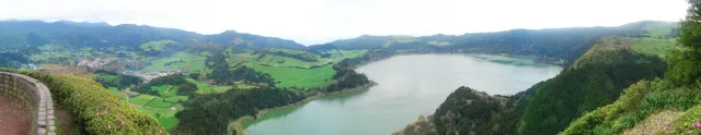 A green volcanic valley with a still lake between wooded slopes