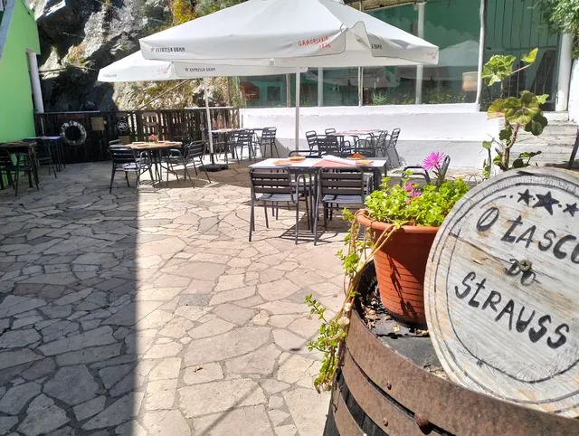 A stone-paved courtyard with tables under white umbrellas and a flower pot on a barrel