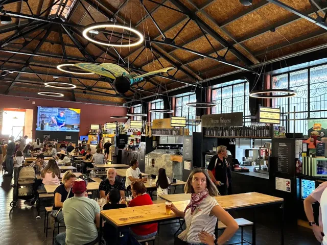 A hall with a beamed roof, ring lamps and long wooden tables full of diners