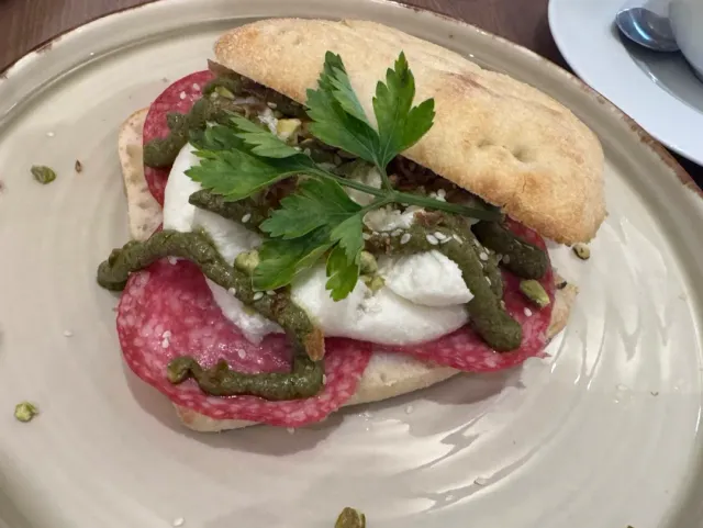 An open sandwich on rustic bread with sausage, white cheese, green sauce and parsley leaves
