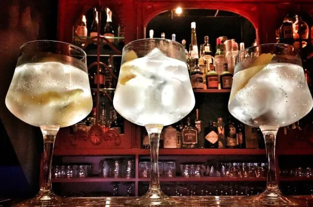 Three gin goblets on a counter facing bottle shelves in red light