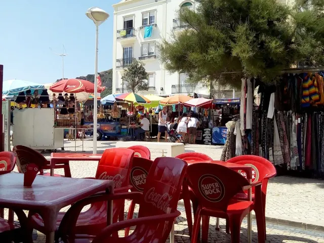 Red plastic chairs on a paved square facing stalls with colourful parasols